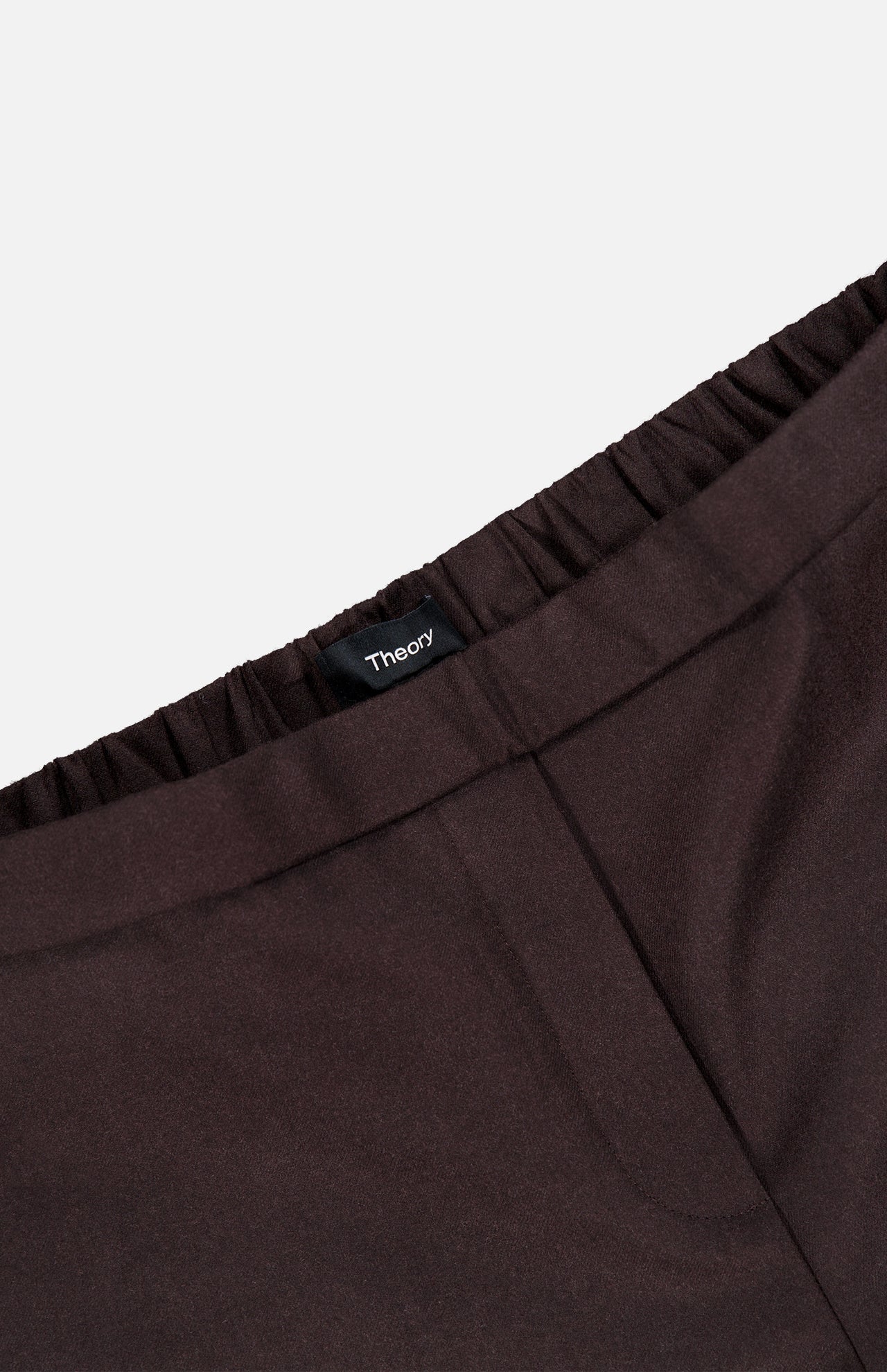 Close-up of the waistband of a pair of chocolate brown Treeca Pull-On Pants with an elastic waist and a THEORY brand tag visible at the center. The background is plain white, highlighting these stylish slim fit wool pants—perfect for sophisticated office attire.