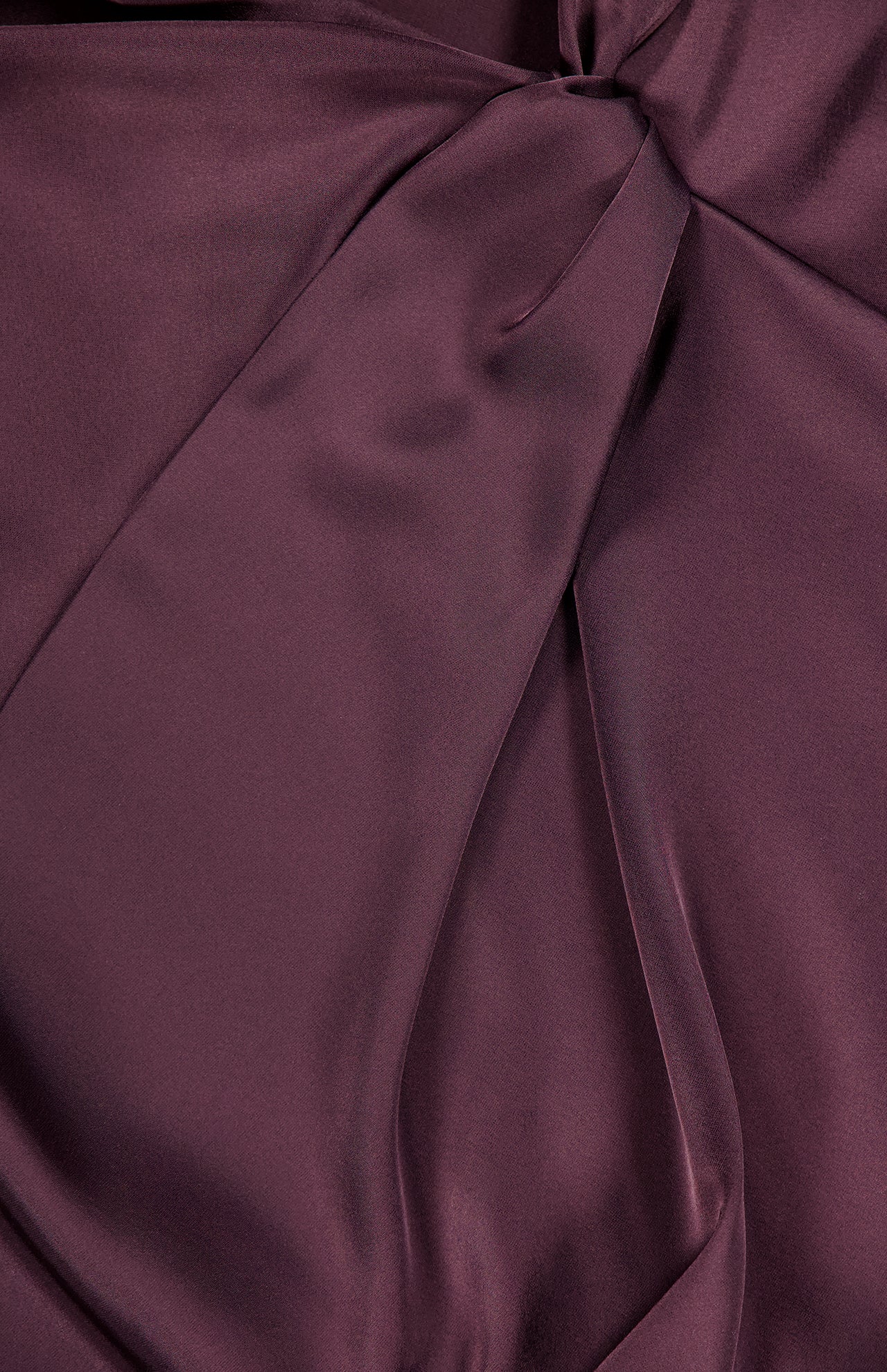 A close-up of THEORY’s Twist Bodice Midi Dress shows smooth, shiny Japanese double satin in rich plum, with visible knots and gentle folds casting soft shadows and enhancing its luxurious texture.