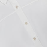 Close-up of the THEORY Yoke Elastic Short Sleeve Shirt in white, highlighting part of the collar, front buttons, and a distinctive diagonal seam across the fabric.