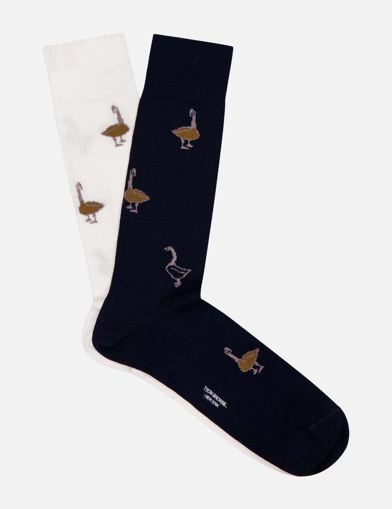 THOM BROWNE’s Fun Mix Geese Half Drop Jacquard Mid Calf Socks, crafted from 100% cotton, feature one white and one dark blue sock, each adorned with brown and beige geese patterns, shown side by side on a white background.