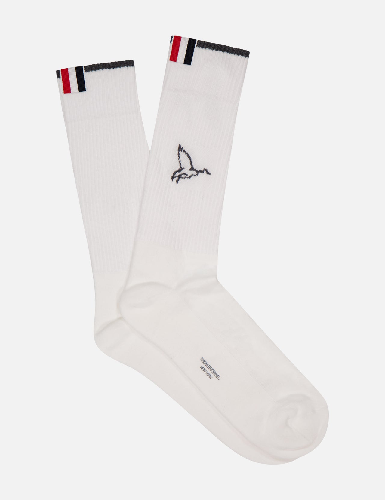 The THOM BROWNE Geese Icon Over The Calf Athletic Socks are white stretch cotton crew socks with a small embroidered bird and red, white, and navy Americana-inspired stripes on the ribbed cuffs, shown flat on a plain white background.