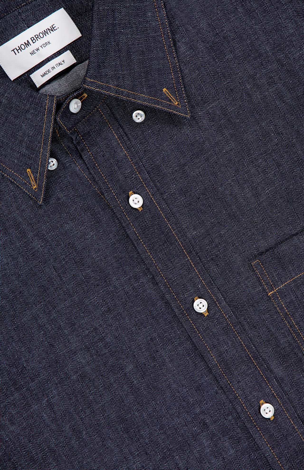 A close-up of the THOM BROWNE Denim Long Sleeve Button Down Straight Fit Shirt in dark cotton denim with white buttons, orange stitching, a pointed collar, and chest pocket—expertly made in Italy for a timeless Americana look.