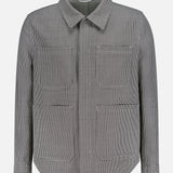 The THOM BROWNE Houndstooth Utility Patch Pocket Jacket features a black and white houndstooth pattern, a collared neckline, concealed front zipper with placket, and two large front pockets, shown on a white background.