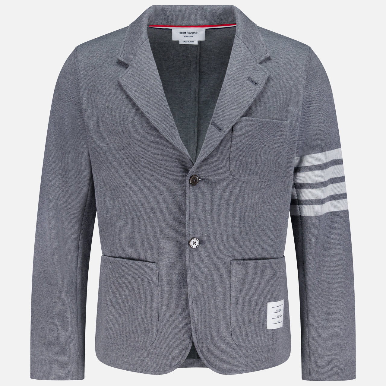 The THOM BROWNE Cotton Knit Sack Jacket is a grey single-breasted sportcoat with two buttons, three white stripes on the left sleeve, three front pockets, and a signature white label above the right pocket hem.
