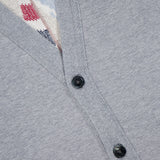 Close-up of THOM BROWNE’s Stitched Boat Graphic Cardigan in light grey, styled as a men’s Americana piece with two black buttons. A patterned knit top in red, blue, and beige is visible under the cardigan opening.
