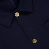 Close-up of a dark navy Compact Milano Car Jacket by THOM BROWNE, featuring gold engraved buttons, a pointed collar, and the brand’s label at the neckline—an elevated take on classic Americana style.
