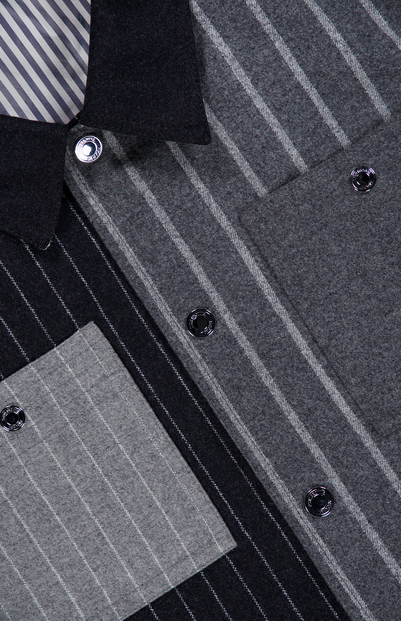 Close-up of the Funmix Stripe Utility Patch Pocket Jacket by THOM BROWNE, featuring a mix of striped patterns and angles in shades of gray and black. This elevated staple in American menswear showcases its multi-textured design with button closures, a classic collar, and utility patch pockets.