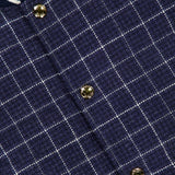 Close-up of the Houndstooth Teviot Tweed Snap Front Vest by THOM BROWNE, featuring a blue and white check pattern, gold snap buttons, and a collar detailed with navy, white, and striped trim—expertly combining down-filled comfort with classic American style.