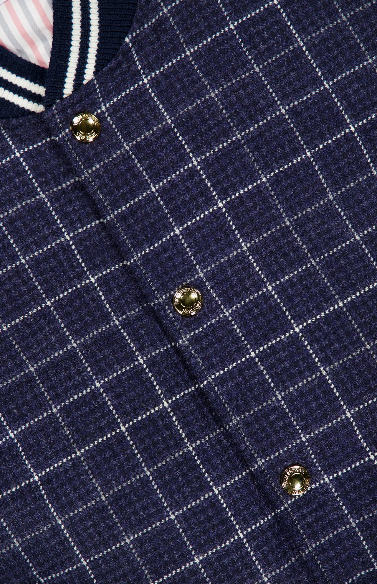 Close-up of the Houndstooth Teviot Tweed Snap Front Vest by THOM BROWNE, featuring a blue and white check pattern, gold snap buttons, and a collar detailed with navy, white, and striped trim—expertly combining down-filled comfort with classic American style.