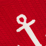 Introducing the Intarsia Anchor Merino Wool Crew Neck Sweater by THOM BROWNE—a vibrant red cable-knit sweater crafted from fine merino wool, featuring a bold white anchor intarsia on the front for a signature nautical flair. A label at the neckline reads “THOM BROWNE. NEW YORK. MADE IN ITALY.”.