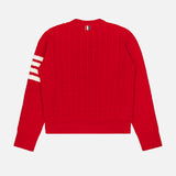 The THOM BROWNE Intarsia Anchor Merino Wool Crew Neck Sweater, a bright red cable-knit men’s sweater with long sleeves, features three white stripes on the left sleeve and a small striped tag at the back neckline. It is displayed laid flat on a white background.