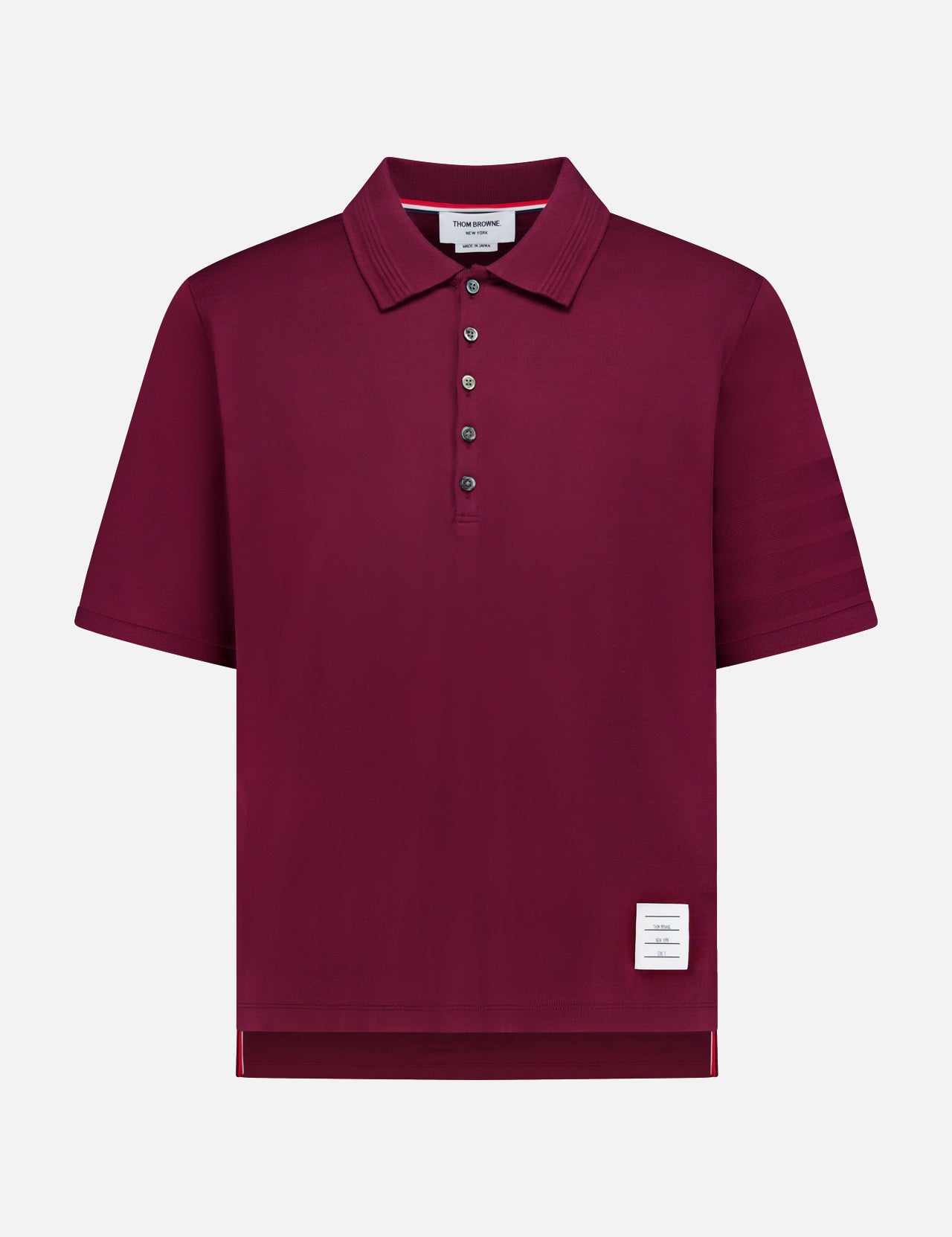 The THOM BROWNE Jersey Short Sleeve Rib Cuff Polo Shirt, a men's classic in burgundy, showcases a smart collar, five-button placket, ribbed cuffs, and a signature small white label near the bottom hem. Presented against a plain white background.