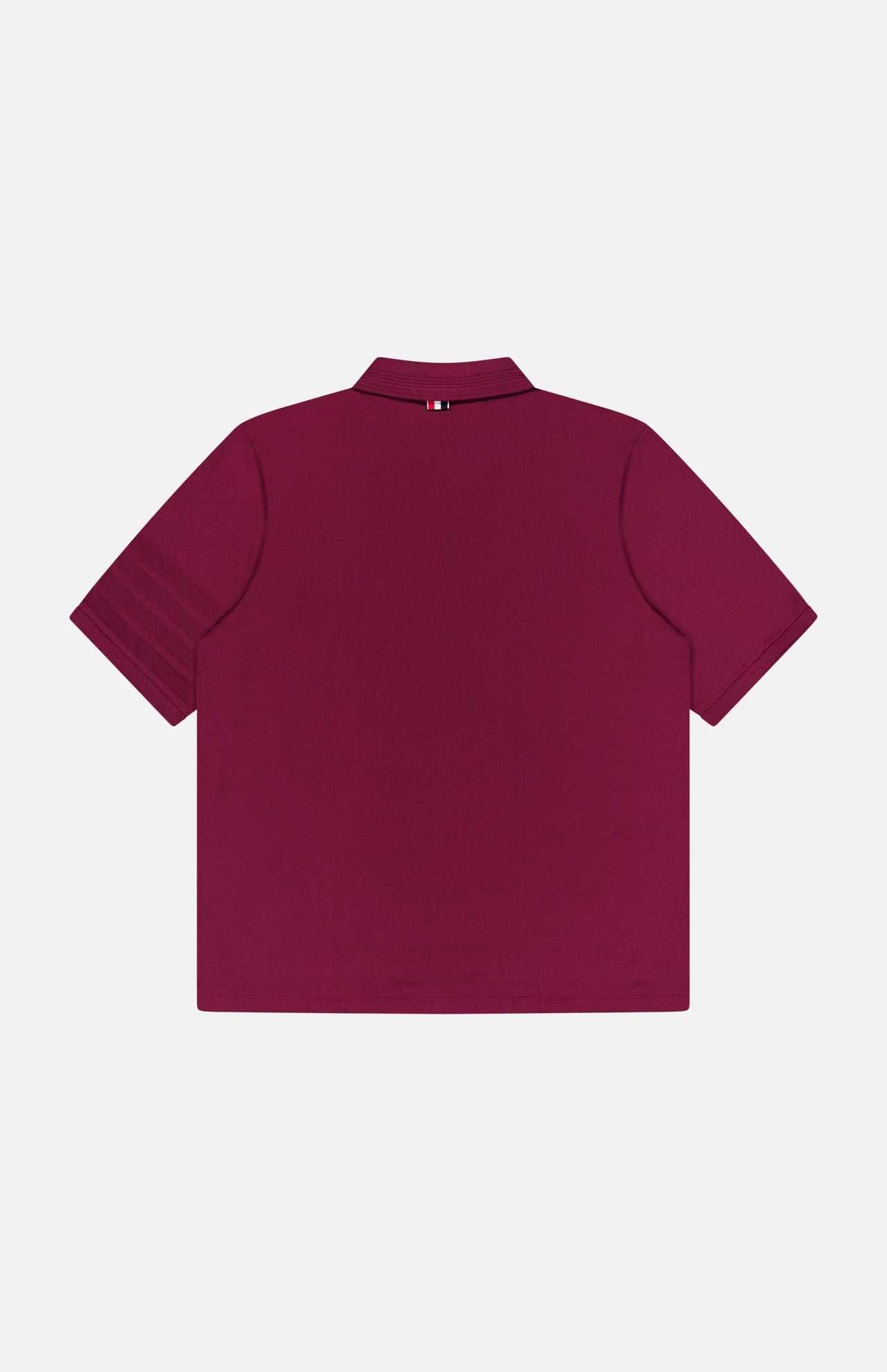 A burgundy THOM BROWNE Jersey Short Sleeve Rib Cuff Polo Shirt is displayed from the back, highlighting its collar and a small striped tag at the neck. This men's polo showcases classic Americana style and is shown laid flat on a white background.