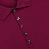 Close-up of the THOM BROWNE Jersey Short Sleeve Rib Cuff Polo Shirt in rich burgundy, detailed with five black buttons and a visible white collar tag reading “THOM BROWNE. NEW YORK. MADE IN JAPAN”—a refined nod to classic Americana style.