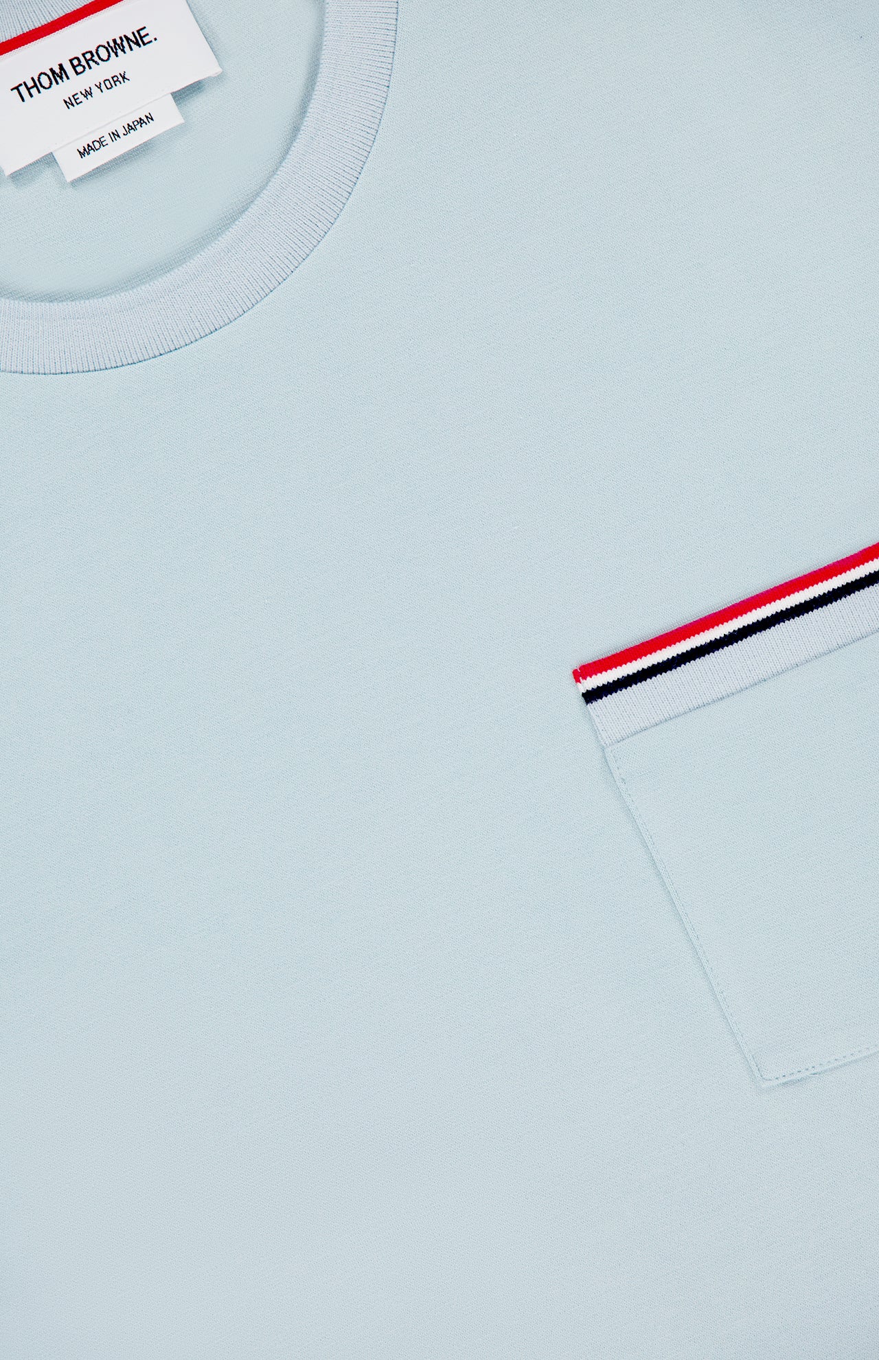 The Milano Cotton Pocket Short Sleeve T-shirt by THOM BROWNE updates Americana style with a light blue cotton tee, red, white, and navy striped trim, chest pocket, and signature label at the collar.