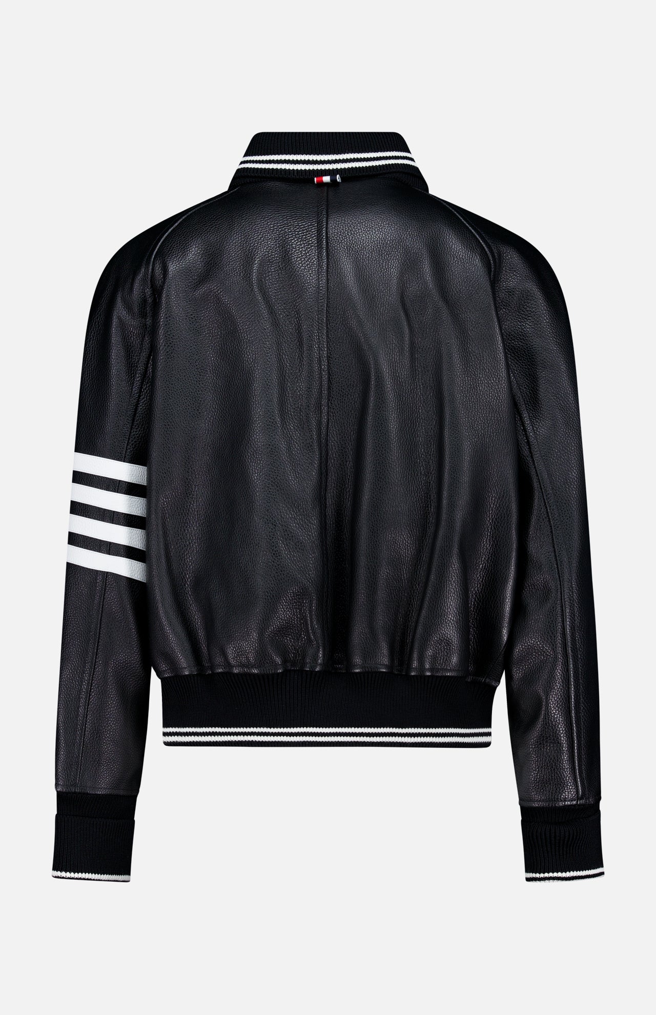 The Oversized Deerskin Leather Bomber Jacket by THOM BROWNE, shown from the back, is black with an oversized varsity style, white stripe on one sleeve, ribbed cuffs and hem, and a small red, white, and blue Americana logo on the collar.