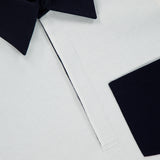 Close-up of the THOM BROWNE Oversized Long Sleeve Colorblock Rugby Polo Shirt, showcasing a white body contrasted by a dark navy collar and sleeve cuffs in an elegant colorblock design. The visible label reads “THOM BROWNE. NEW YORK. MADE IN ITALY,” and the placket is neatly stitched in white.