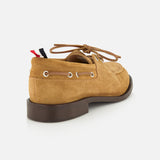 The Padded Boat Suede Loafer by THOM BROWNE is a tan men’s slip-on with brown laces, metal eyelets, decorative stitching, and a thick dark brown sole, shown from the back against a white background.
