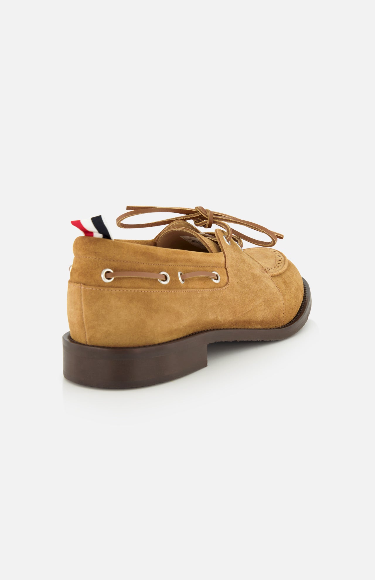 The Padded Boat Suede Loafer by THOM BROWNE is a tan men’s slip-on with brown laces, metal eyelets, decorative stitching, and a thick dark brown sole, shown from the back against a white background.
