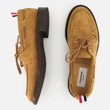 The THOM BROWNE Padded Boat Suede Loafers in tan feature brown soles, beige laces, and signature red, white, and blue striped heel tabs. Displayed against a white background, one is shown from the side and one from above.