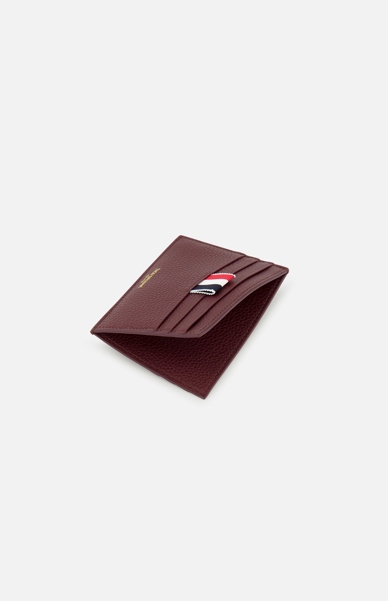 The THOM BROWNE Pebble Grain Leather Card Holder for men, in burgundy leather with multiple card slots and a signature red, white, and black front fabric detail, is shown against a light gray background.