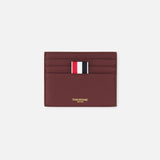 The THOM BROWNE Pebble Grain Leather Card Holder, in burgundy leather, features four card slots, a central red, white, and navy striped fabric tab, and gold branding below the slots. Shown here on a plain white background.