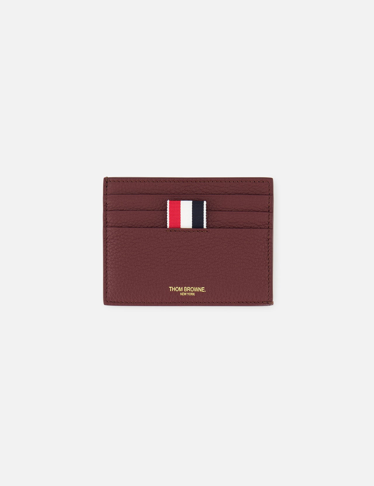 The THOM BROWNE Pebble Grain Leather Card Holder, in burgundy leather, features four card slots, a central red, white, and navy striped fabric tab, and gold branding below the slots. Shown here on a plain white background.