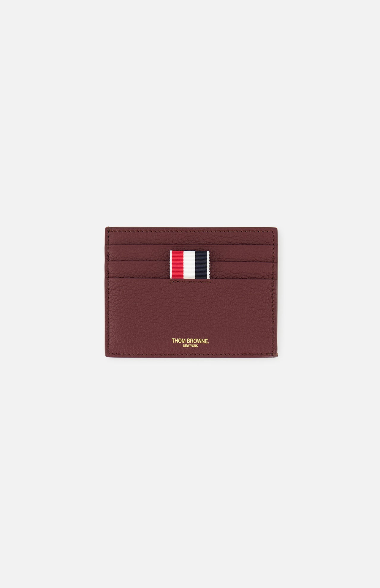 The THOM BROWNE Pebble Grain Leather Card Holder, in burgundy leather, features four card slots, a central red, white, and navy striped fabric tab, and gold branding below the slots. Shown here on a plain white background.