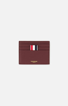 The THOM BROWNE Pebble Grain Leather Card Holder, in burgundy leather, features four card slots, a central red, white, and navy striped fabric tab, and gold branding below the slots. Shown here on a plain white background.