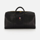 The THOM BROWNE Pebble Grain Leather Duffle Bag features black leather, gold zippers and hardware, two handles, and a front logo with red, white, and blue stripes—a stylish and convenient travel essential.