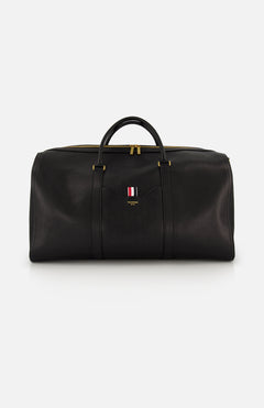 The THOM BROWNE Pebble Grain Leather Duffle Bag features black leather, gold zippers and hardware, two handles, and a front logo with red, white, and blue stripes—a stylish and convenient travel essential.