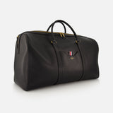The THOM BROWNE Pebble Grain Leather Duffle Bag is a spacious black travel essential in premium leather with gold zipper, dual handles, and a small pocket accented by the brand's signature red, white, and blue striped detail.