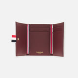 The Pebble Grain Leather Trifold Wallet by THOM BROWNE features burgundy leather, gold branding inside, two card slots per side, a central pocket, and a red, white, and blue striped tab—a refined men’s accessory for everyday style.