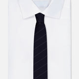 A neatly folded white dress shirt with a crisp collar is paired with the THOM BROWNE Pinstripe Wool Classic Tie—an Italian-made, dark navy tie featuring subtle diagonal pinstripes—displayed against a plain light background.