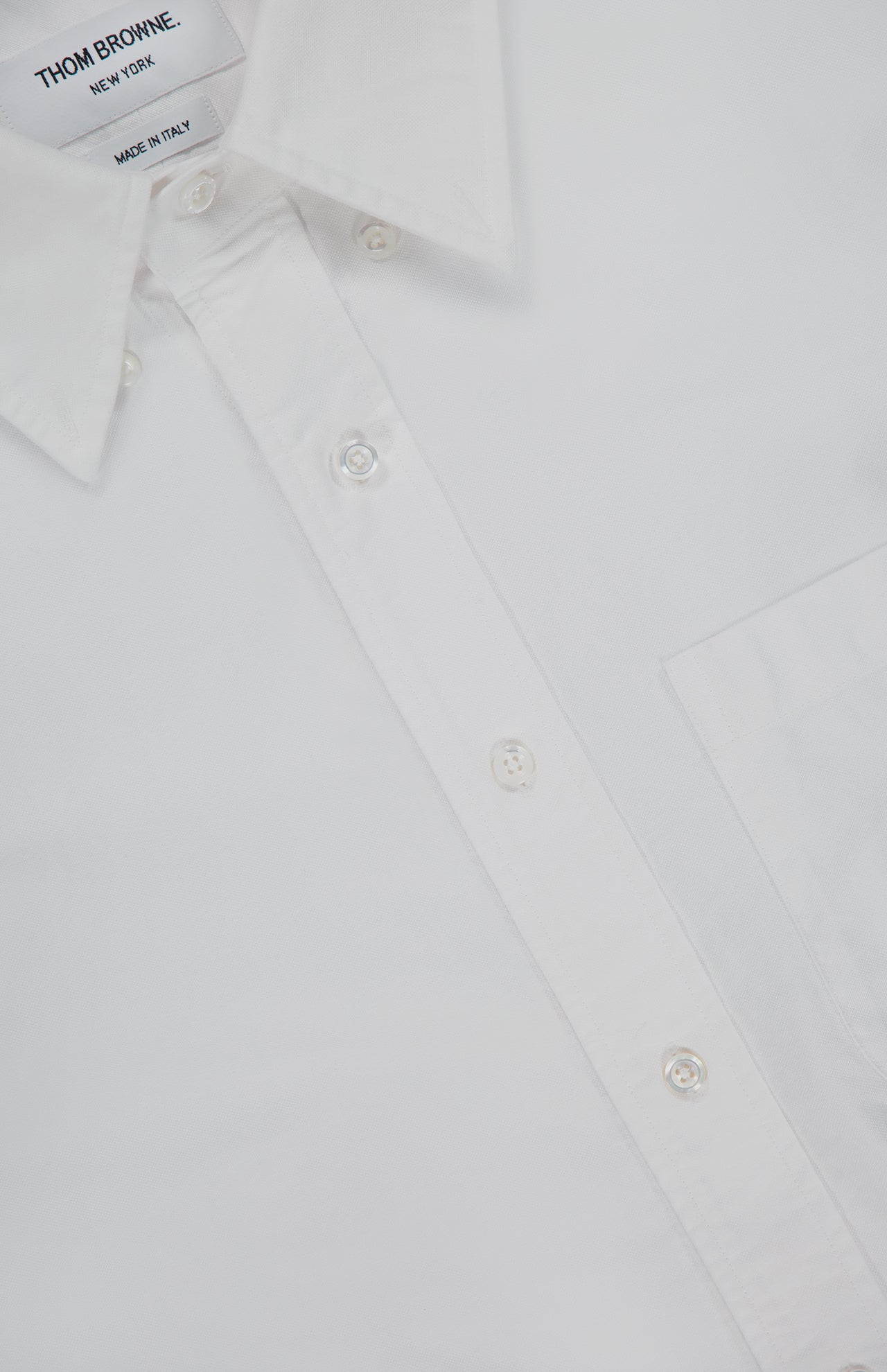 Close-up of the THOM BROWNE Straight Fit 4 Bar Long Sleeve Oxford Shirt featuring a pointed collar, front pocket, white buttons, and inner label—a classic menswear staple.