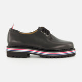 The THOM BROWNE Vitello Calf Leather Derby Loafer is a black polished leather shoe with black laces, moc toe detailing, a thick black sole with a red, white, and black striped trim, and a small heel pull tab. Shown side view on white background.