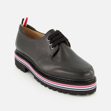 The THOM BROWNE Vitello Calf Leather Derby Loafer is a black moc toe lace-up in polished leather, featuring a thick ridged sole with red, white, and blue stripes and a matching tricolor pull tab at the heel.