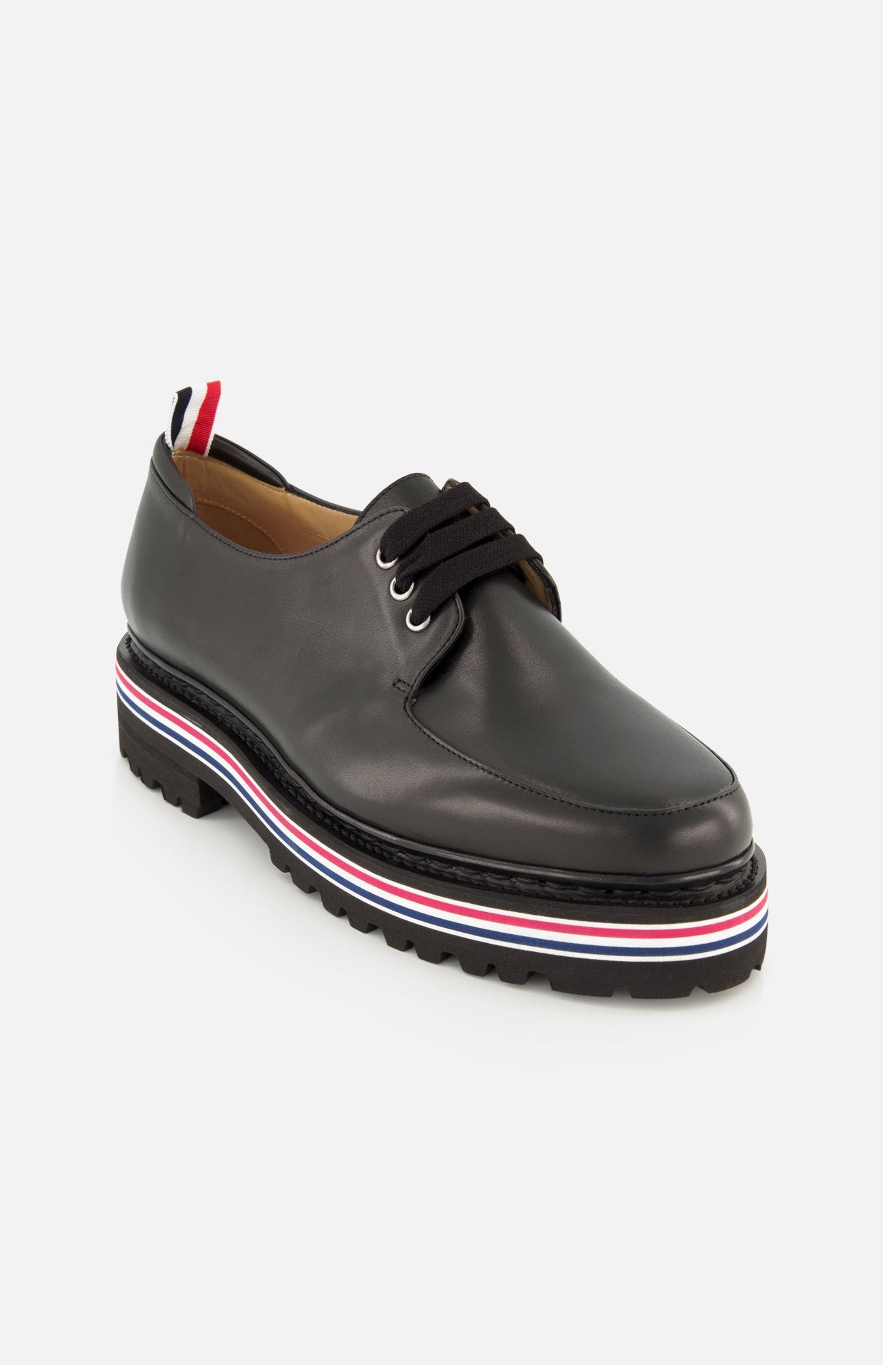 The THOM BROWNE Vitello Calf Leather Derby Loafer is a black moc toe lace-up in polished leather, featuring a thick ridged sole with red, white, and blue stripes and a matching tricolor pull tab at the heel.