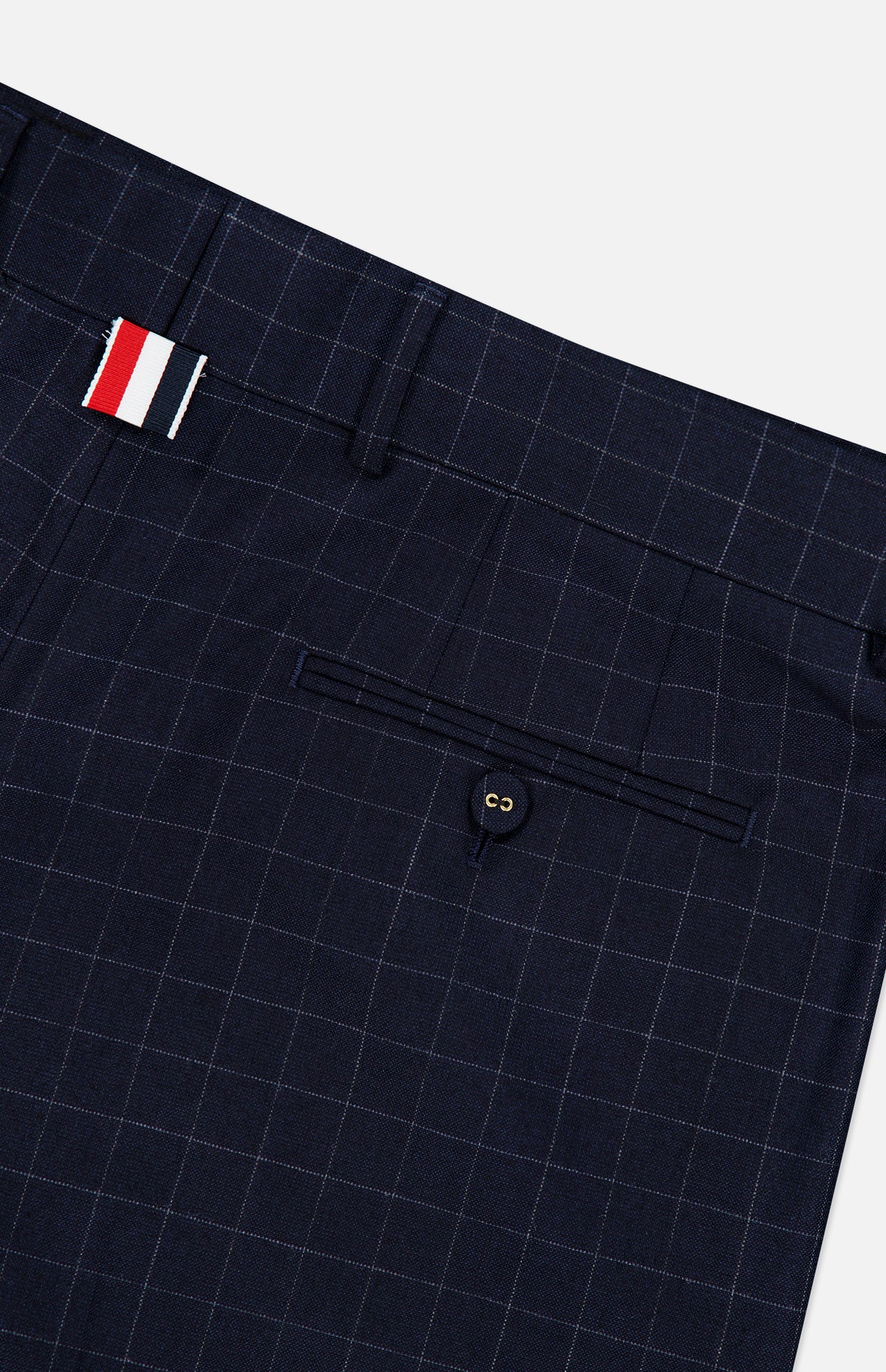 Close-up of THOM BROWNE Windowpane Check Cotton Wool Trouser Pant in navy, featuring a subtle windowpane plaid, single buttoned back pocket, and a belt loop with red, white, and navy stripes.