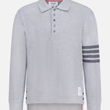 The THOM BROWNE Textured Pique Long Sleeve Polo Shirt features light grey pique cotton, a classic collar, four dark stripes on the left sleeve, side buttons, a buttoned placket, and a signature white label near the hem—a stylish choice for men.