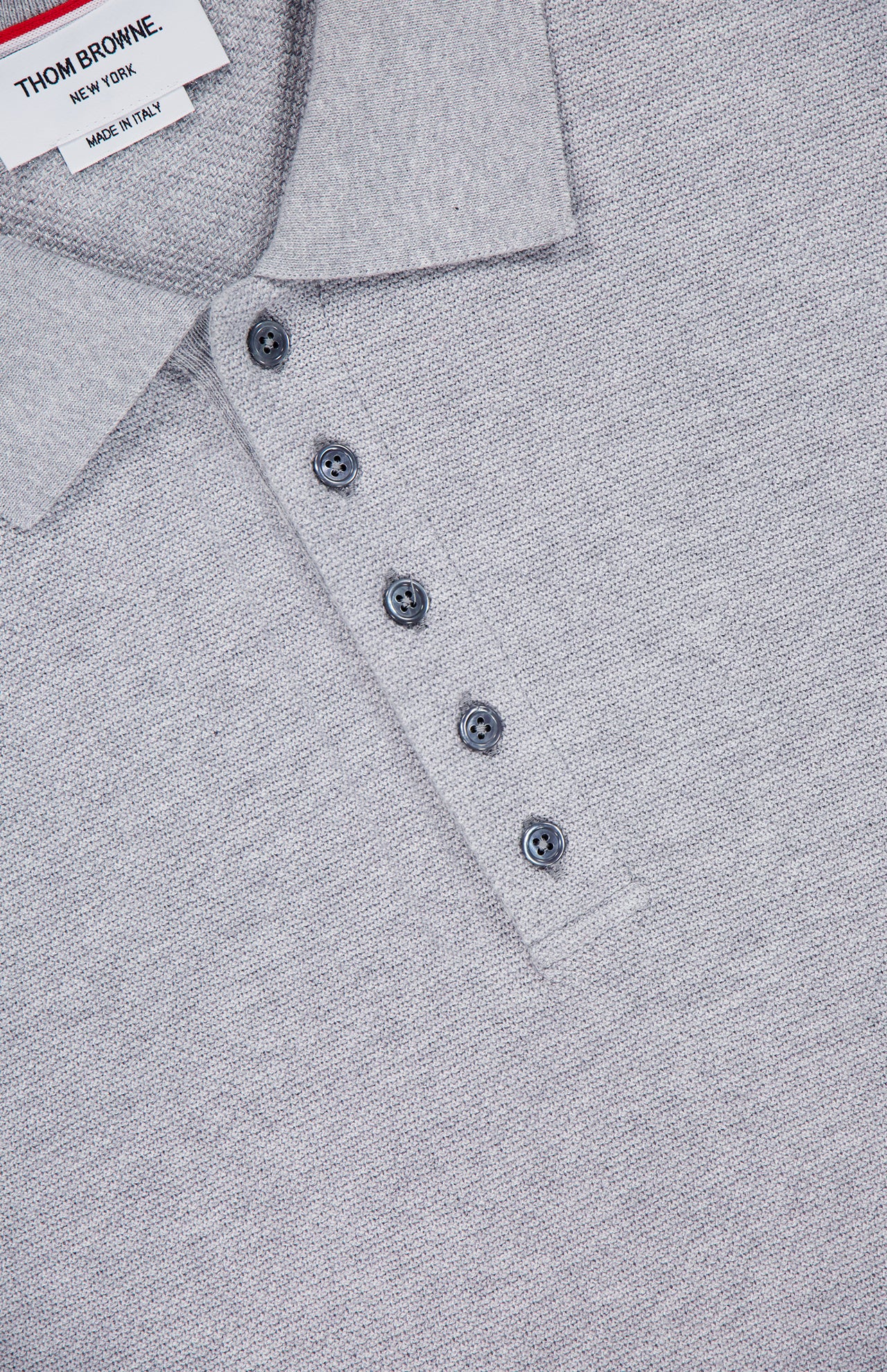 Close-up of the THOM BROWNE Textured Pique Long Sleeve Polo Shirt in light grey, featuring a collar, four dark gray buttons, and a visible brand label inside the neckline.