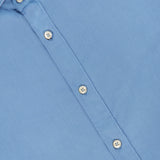 Close-up of the TINTORIA MATTEI Cotton Long Sleeve Dress Shirt in light blue, featuring white buttons and a pointed collar, laid flat. Part of the shirt’s label is visible inside the collar.