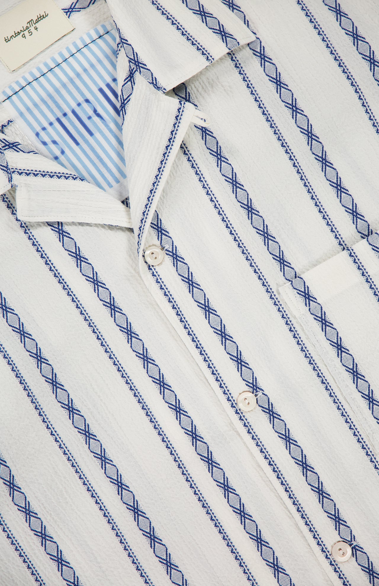 Close-up of the TINTORIA MATTEI Cotton Stretch Short Sleeve Shirt, featuring blue vertical stripes and diamond patterns, a button-down collar, chest pocket, and a visible label at the neckline.