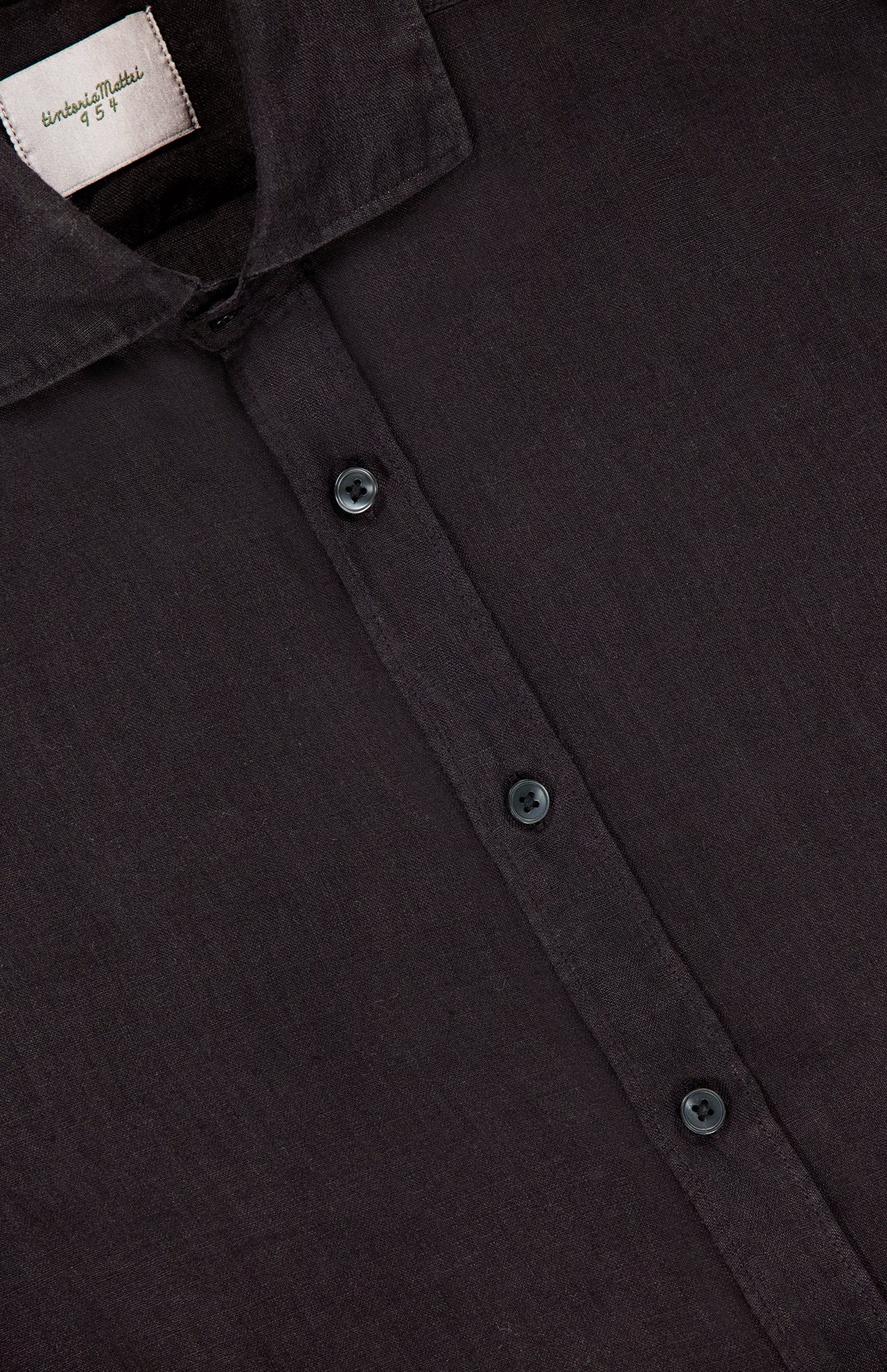 Close-up of the TINTORIA MATTEI Garment Dyed Linen Shirt in black, a summer essential. Features include a soft, slightly textured linen fabric, visible collar, three buttons, and an inner white label with text.
