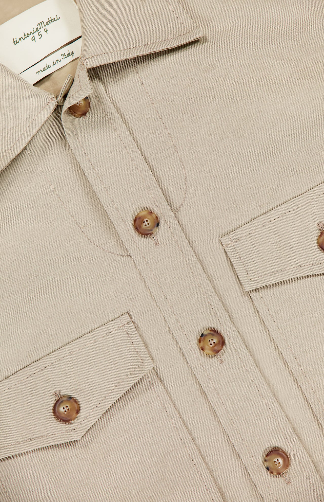 A close-up of the TINTORIA MATTEI Linen and Cotton Overshirt in stone, featuring brown buttons, two chest flap pockets, and a visible label inside the collar, blending casual elegance with refined Italian craftsmanship.