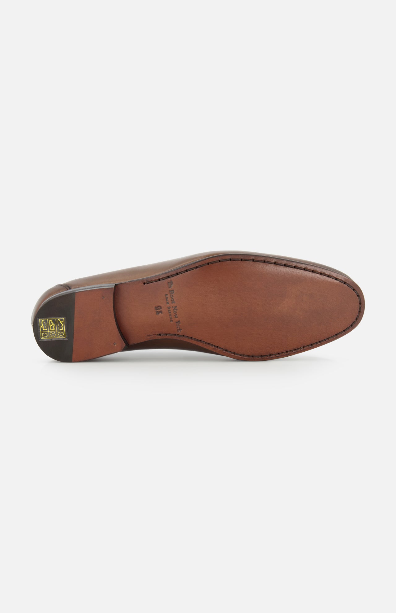 The sole of the Aldrin Leather Penny Loafer by TO BOOT, shown from below, displays smooth brown leather with stitched edges and a small gold and black logo near the heel, reflecting classic Italian loafer style.