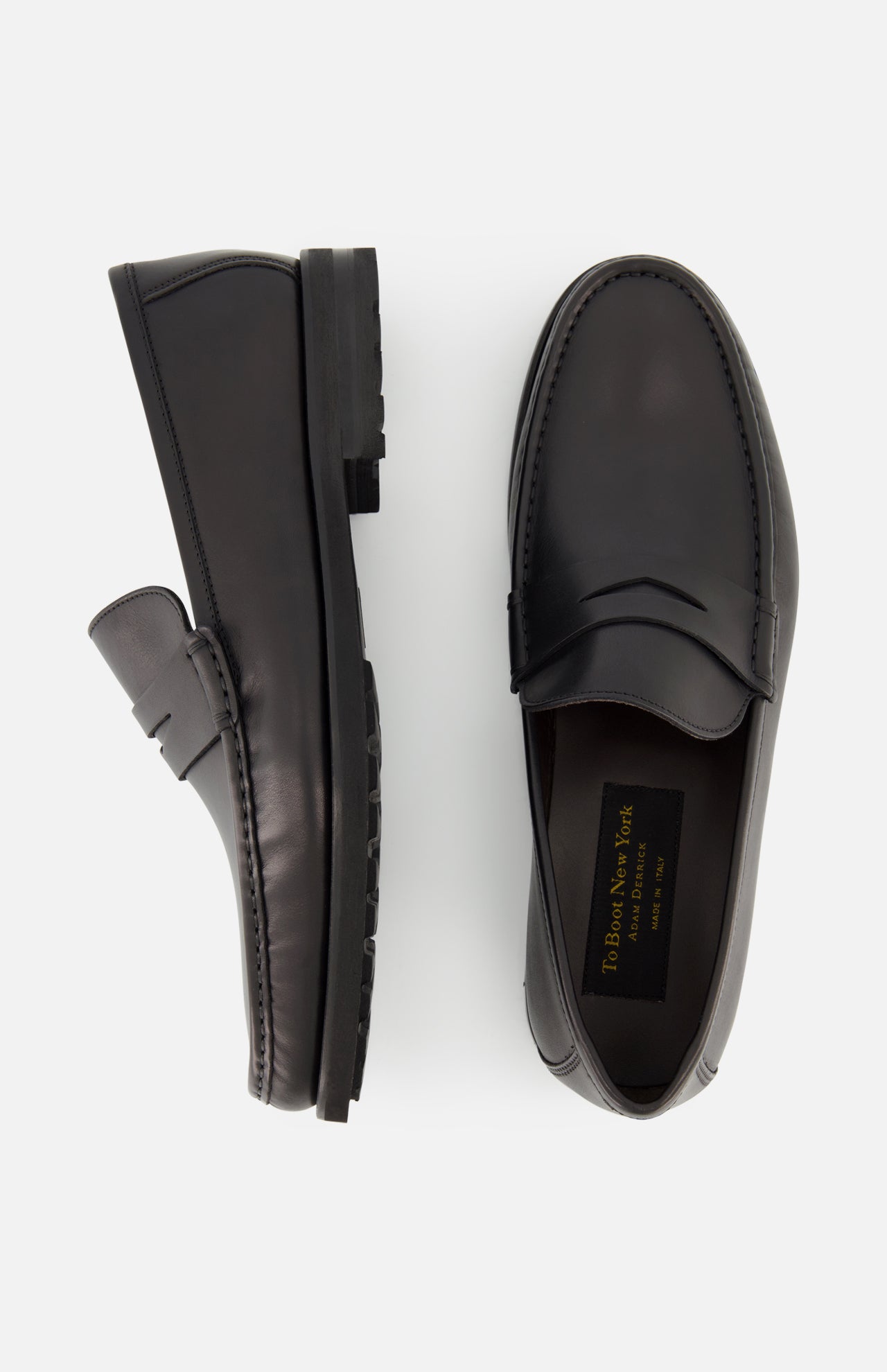 The TO BOOT Belfast Leather Loafer is shown in black leather, one upright and one flat to display the gold branded insole. These sleek, Italian-made loafers feature a low heel and textured sole.