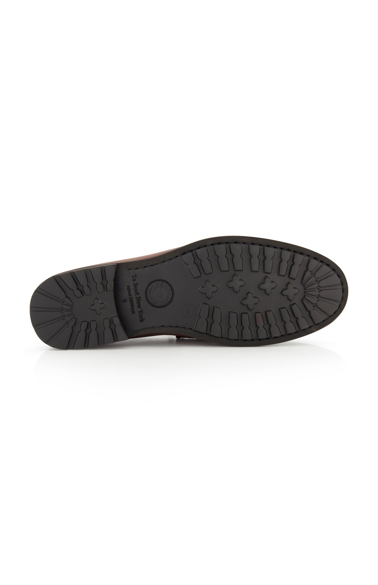 The image displays the bottom view of a black rubber sole featuring textured tread patterns with crosses and lines, engineered for grip and traction, on the TO BOOT Fischer Penny Leather Loafer—a classic slip-on penny loafer crafted from brown leather.