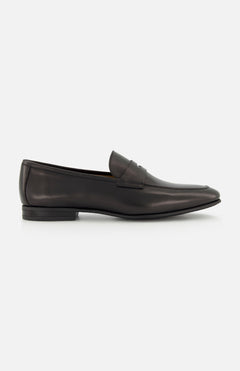 The TO BOOT Keats Leather Penny Loafer is shown in a side profile view against a white background—a single black leather loafer with a low heel and sleek, minimalist design, crafted in the classic tradition of Italian leather loafers.