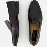 The Keats Leather Penny Loafer by TO BOOT is displayed, with one black leather shoe viewed from the side and the other from above. A tan inner sole featuring a visible TO BOOT brand label highlights these classic slip-on dress shoes.